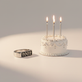 Birthdate ring beside a birthday cake with lit candles